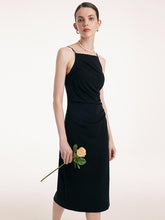 A woman in a mid-length sheath black dress holds a flower in her hand.